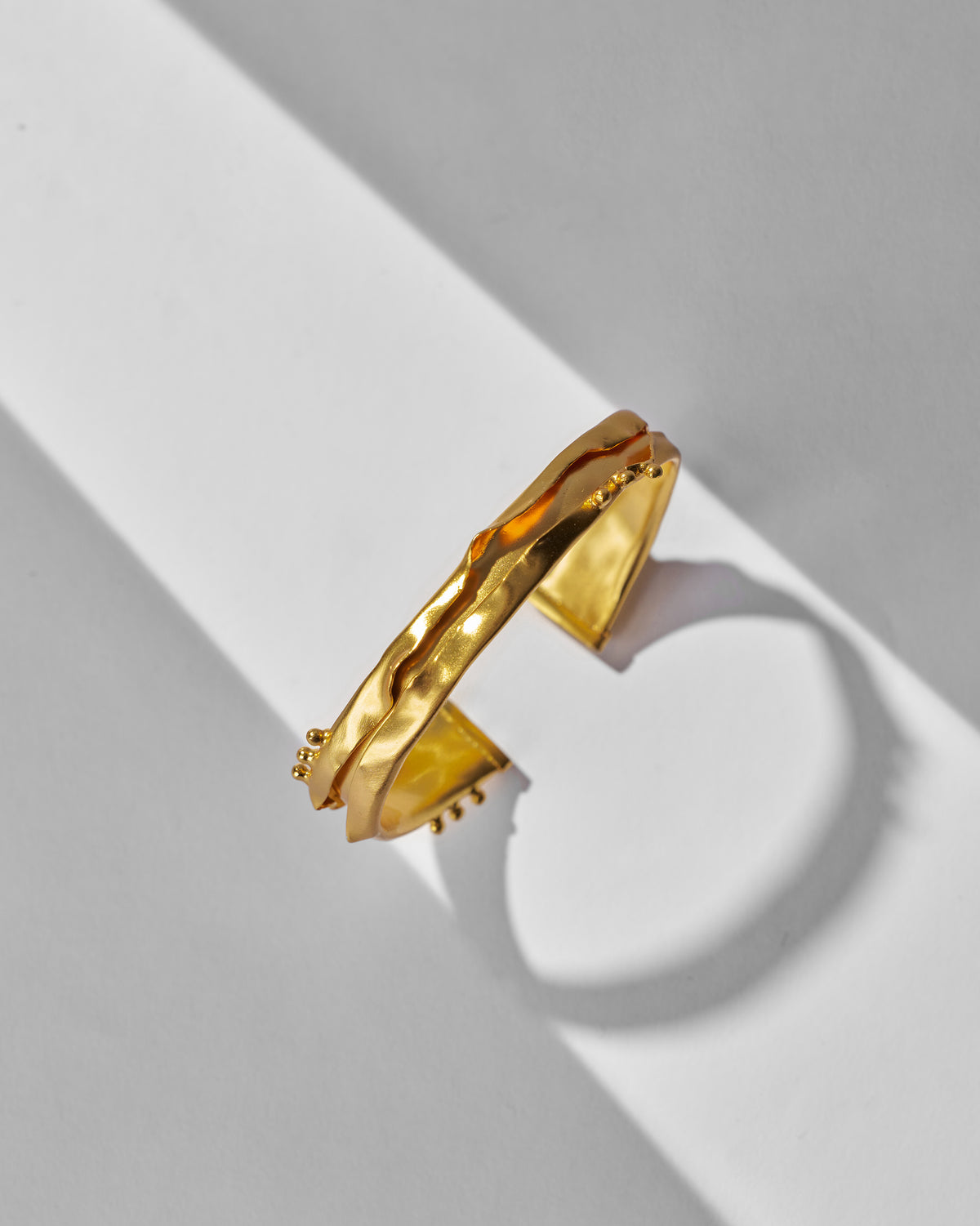 Side view of a gold Dhaara cuff showing its wavy texture.