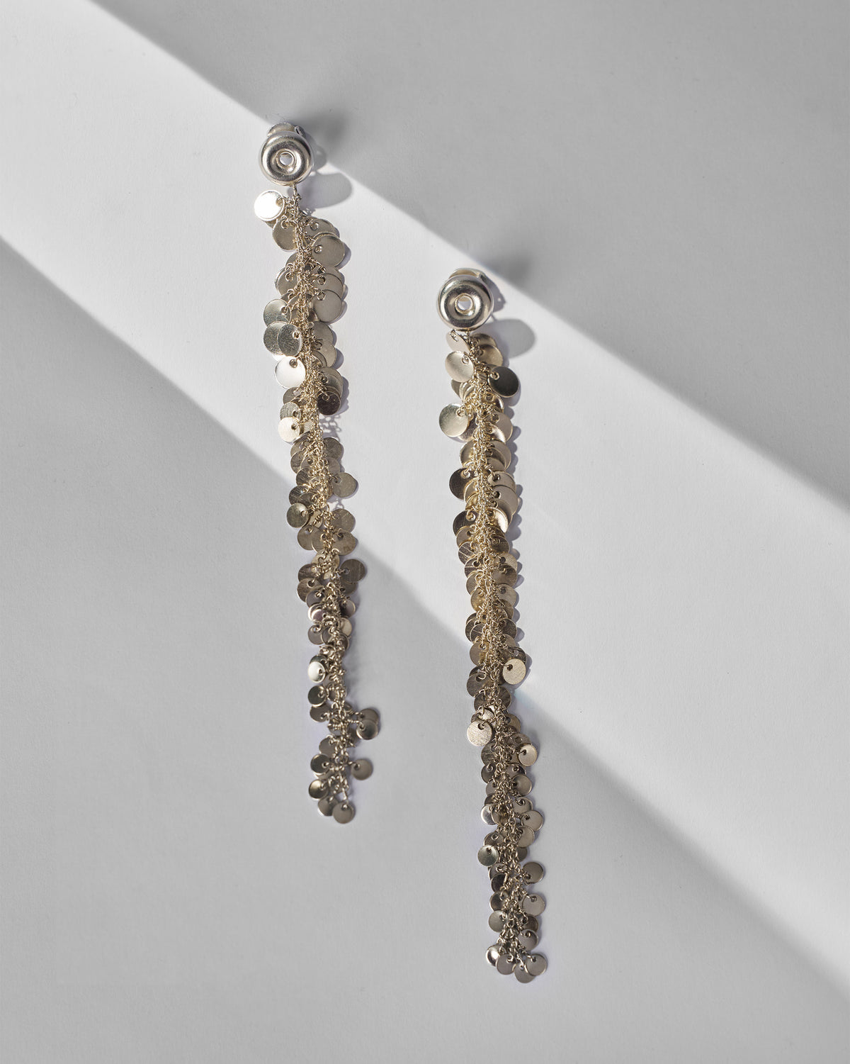 Pair of long silver tassel shoulder duster earrings with disc fringe laid flat.