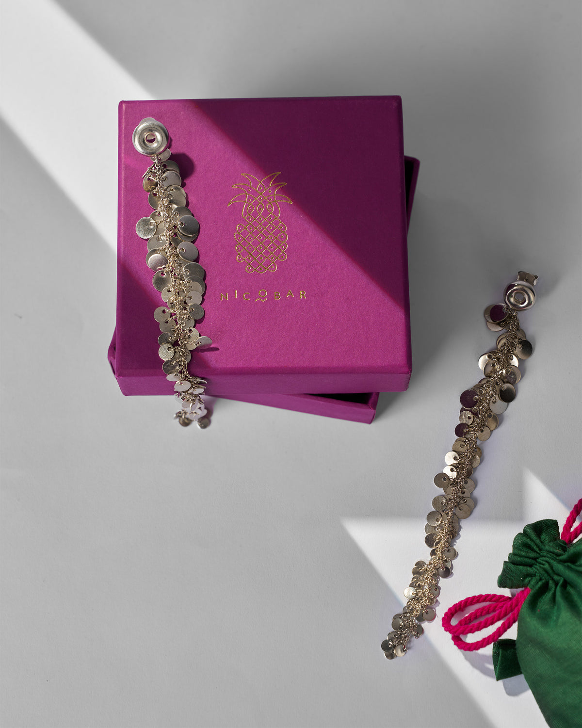 Silver tassel shoulder duster earrings on a magenta Nicobar gift box.