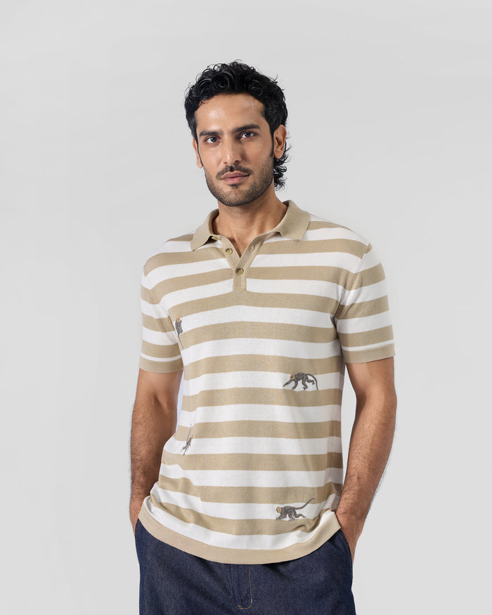 Person wearing an ivory and sand striped Macaque Polo with embroidered monkeys.
