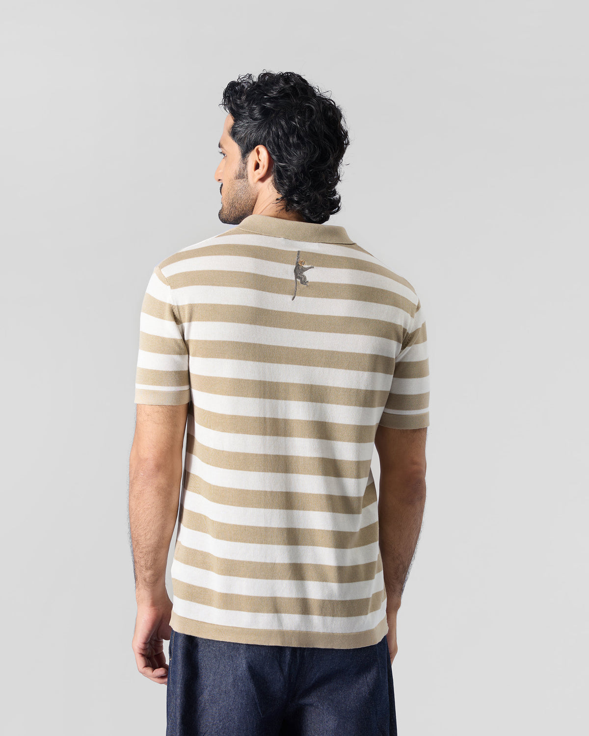 Back of an ivory and sand striped Macaque Polo with an embroidered monkey below the collar.