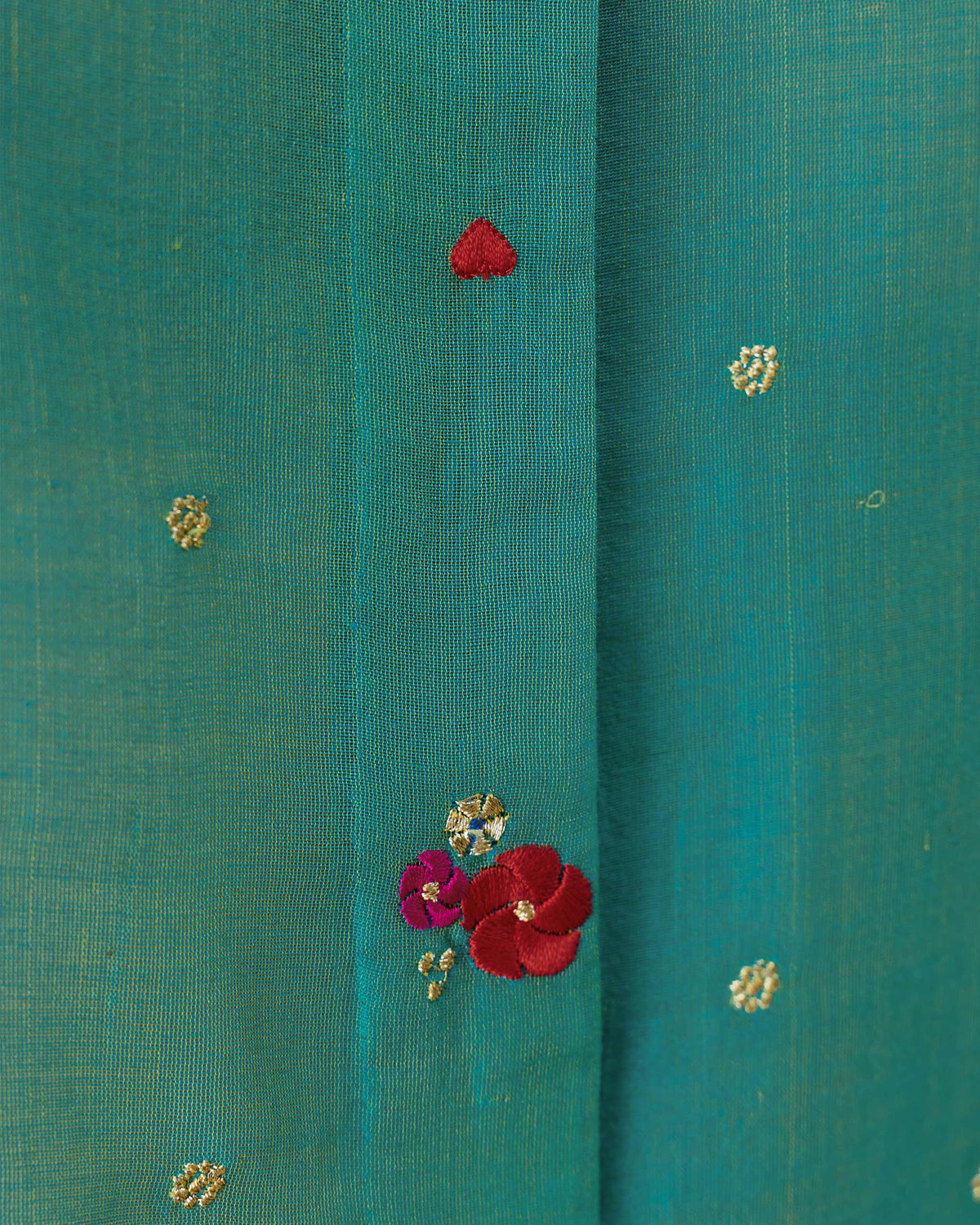 Close-up of floral embroidery and a red heart on an aqua Boxy shirt.