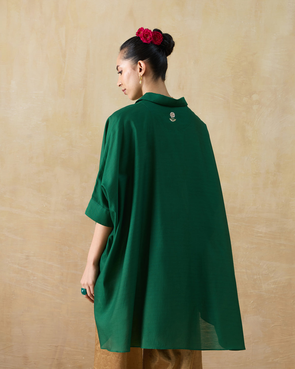 Back of an emerald green Hala tunic with a small gold embroidered flower.