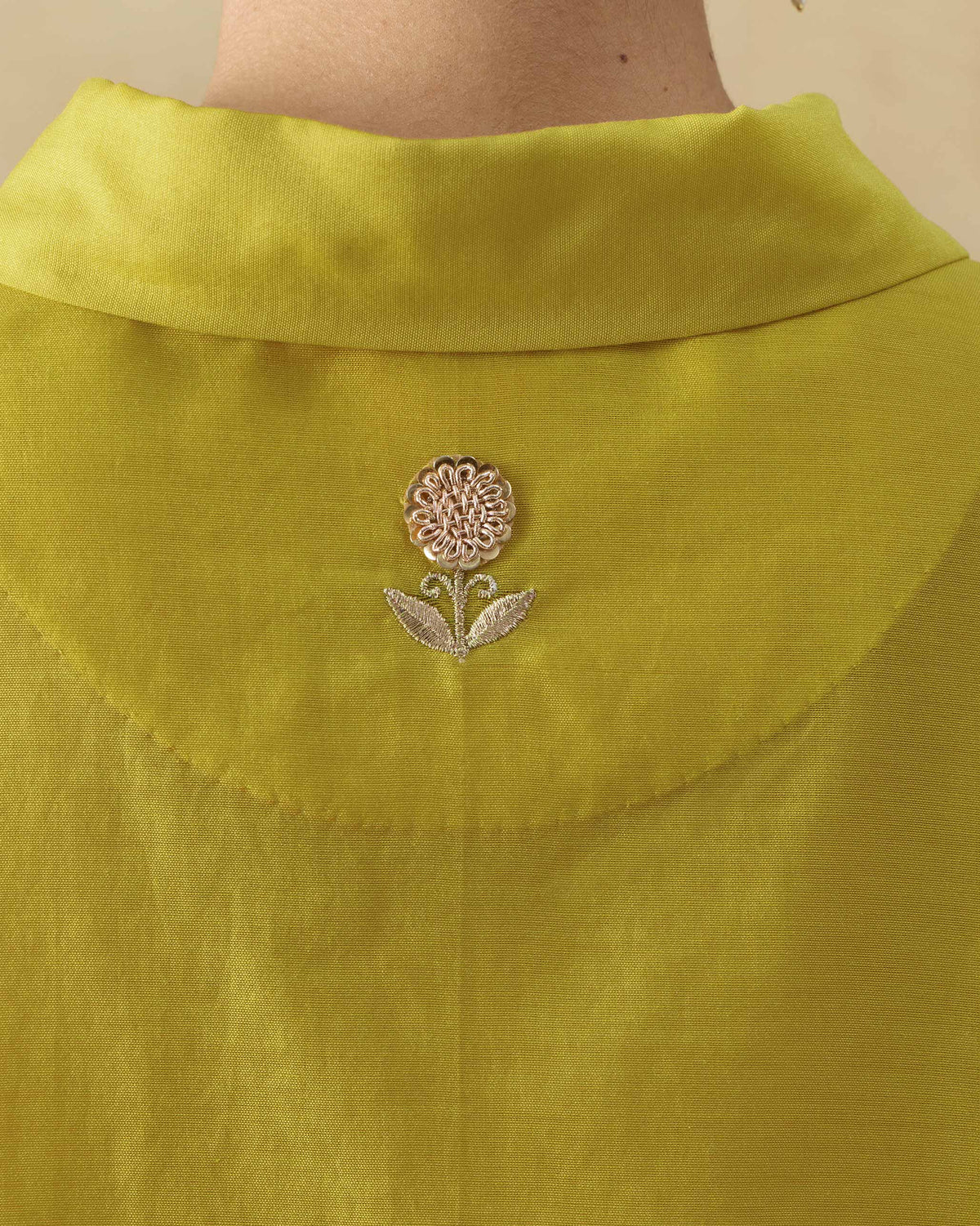 Close-up of a chartreuse tunic with a gold flower on the yoke.