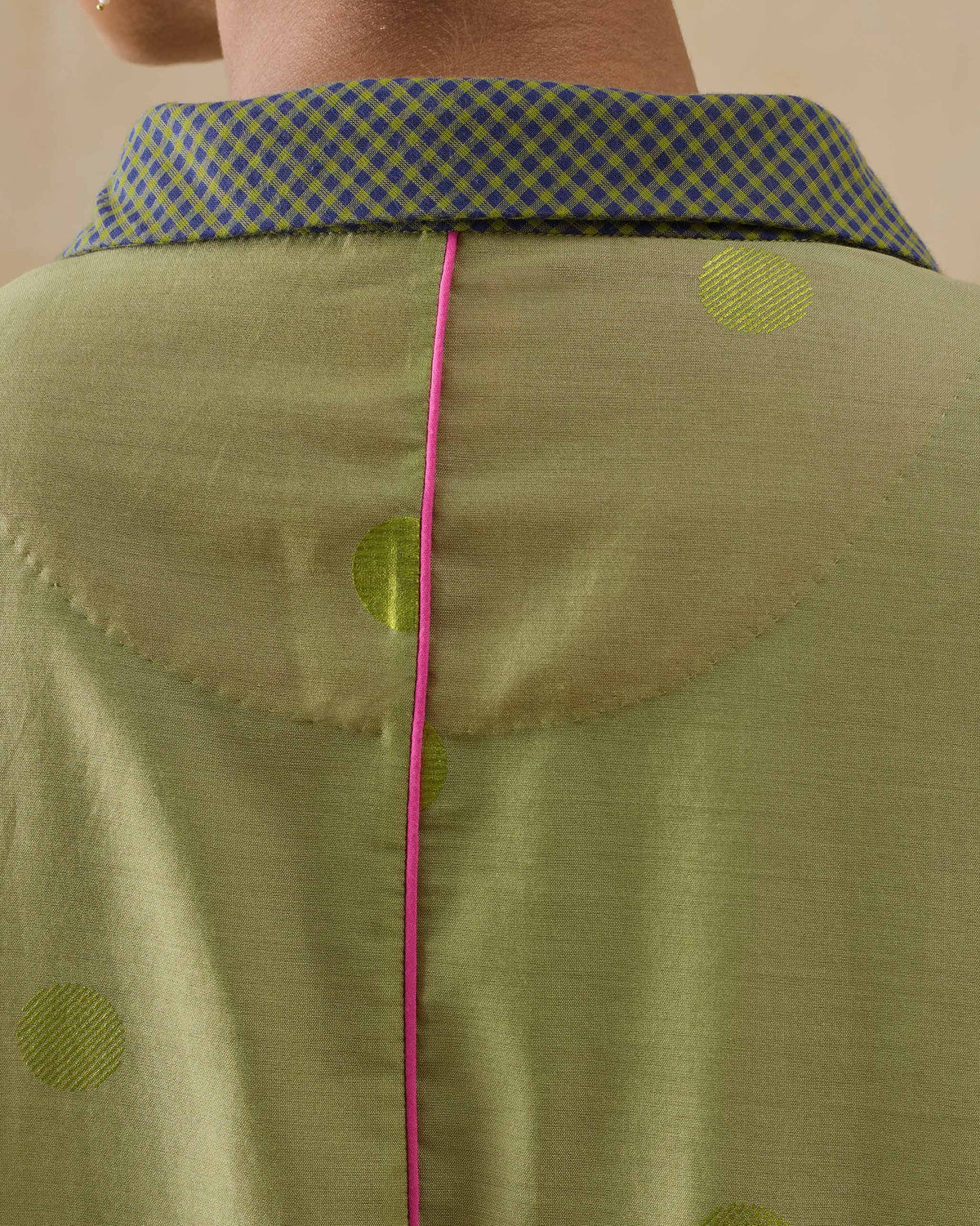 Close-up of a green polka-dot kaftan with pink back piping and a check collar.