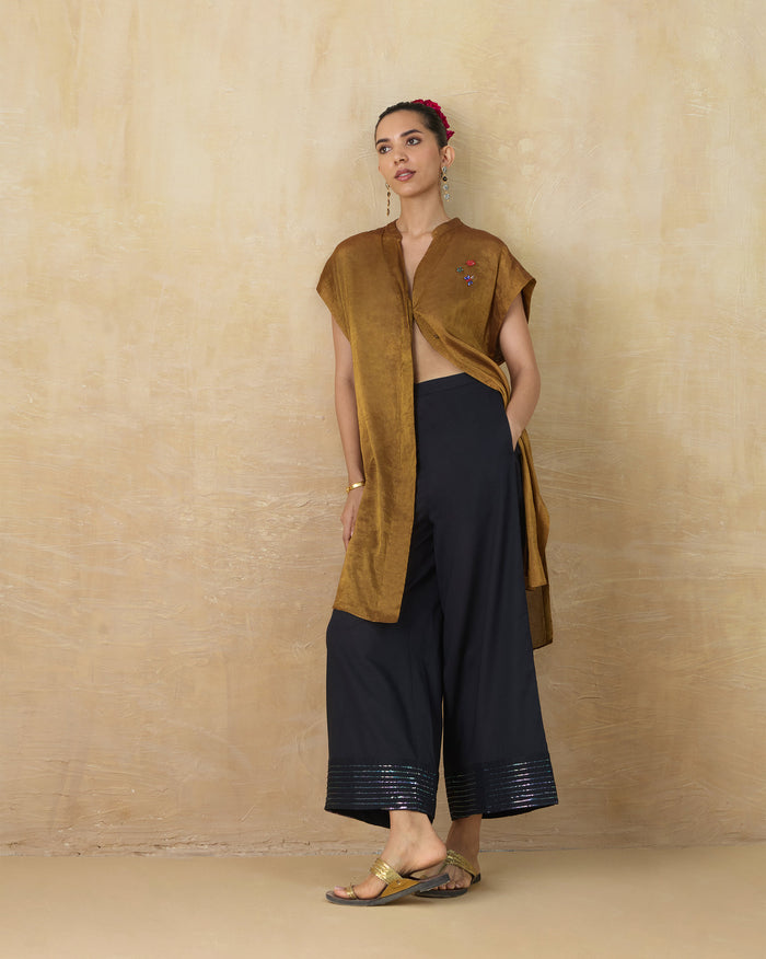 Person wearing a gold metallic Tango kaftan open over navy trousers.
