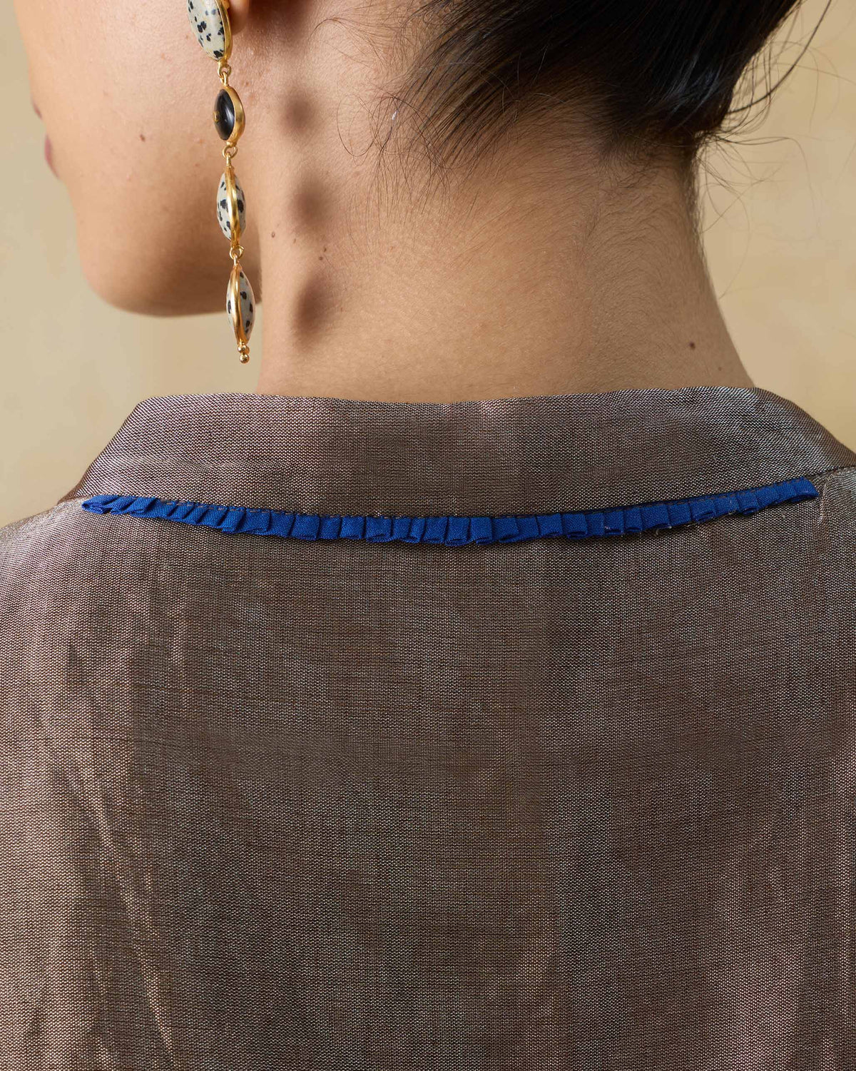 Close-up of a silver metallic kaftan with blue pleated trim at the back neck.