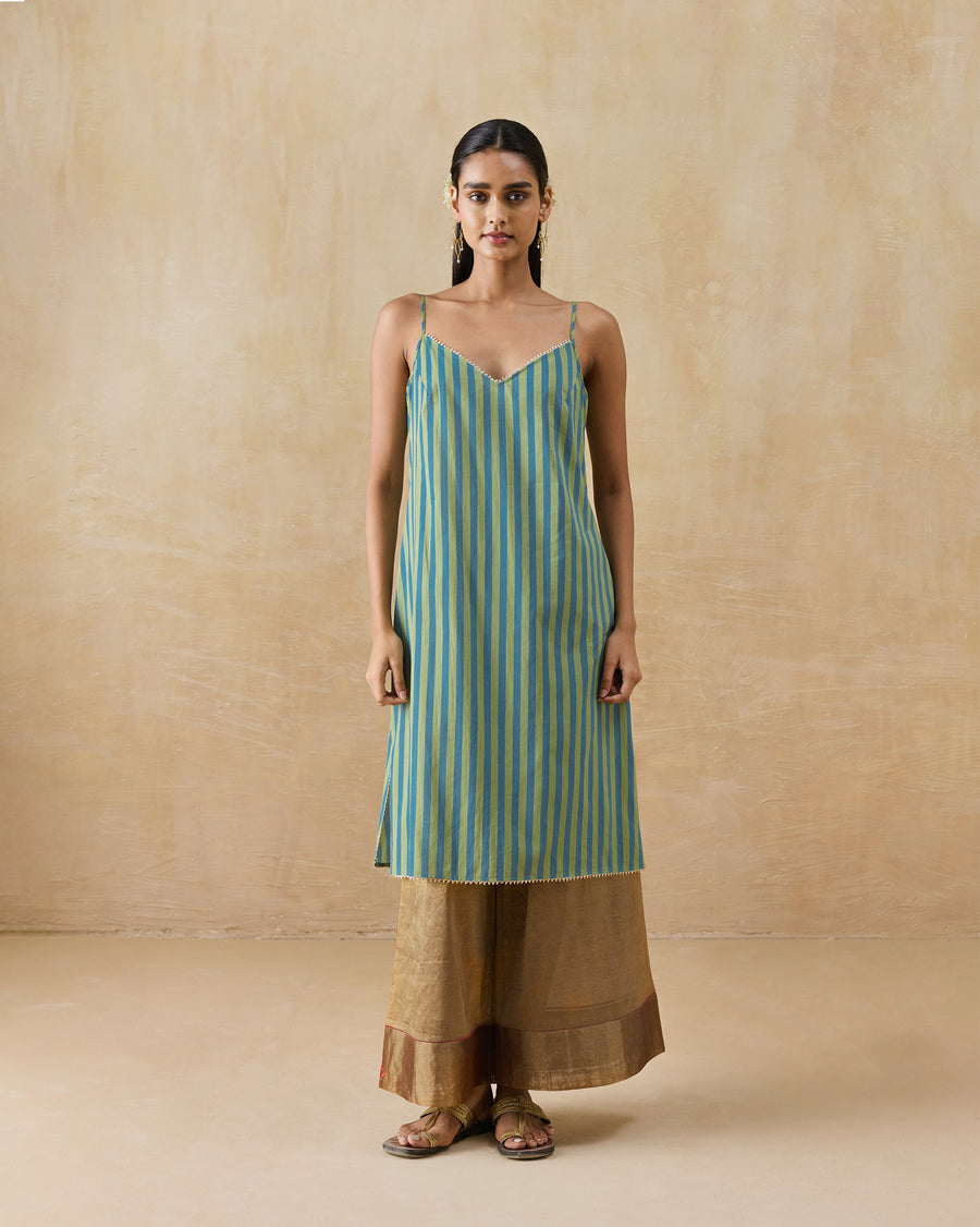 The Mist Camisole, a knee-length green and blue striped voile camisole with a V-neck and thin straps, worn over gold trousers.