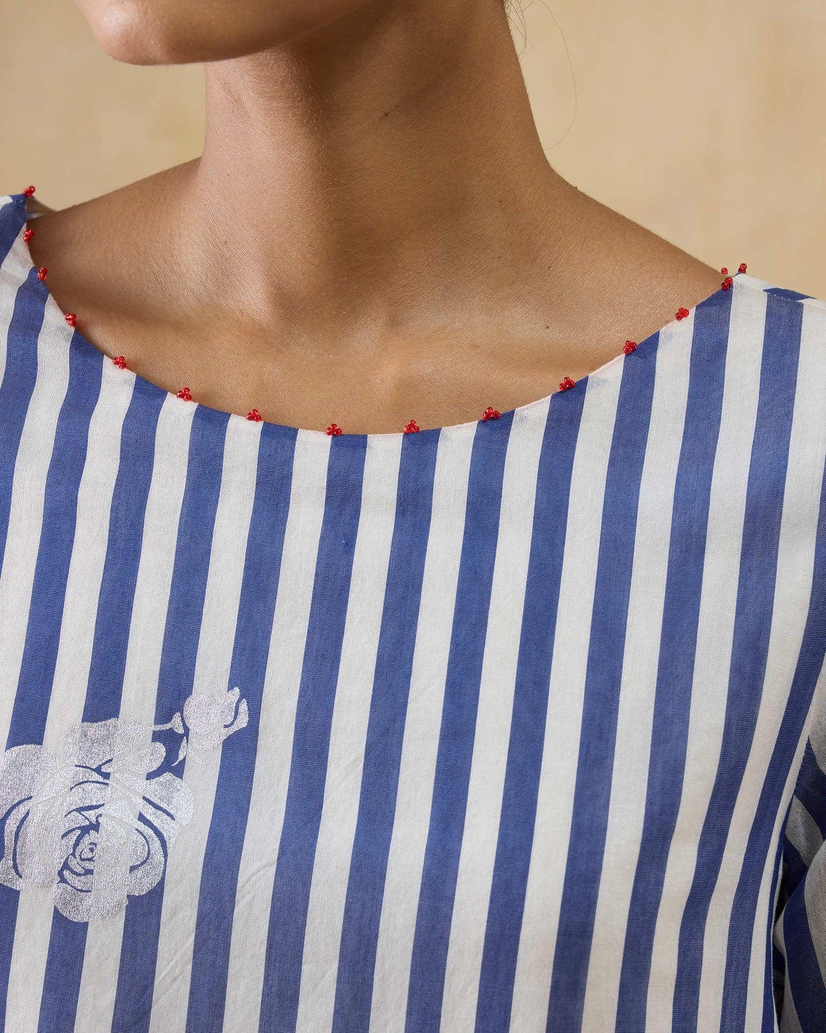 Close-up of a red-beaded boat neck on a cobalt and ivory striped kurta.