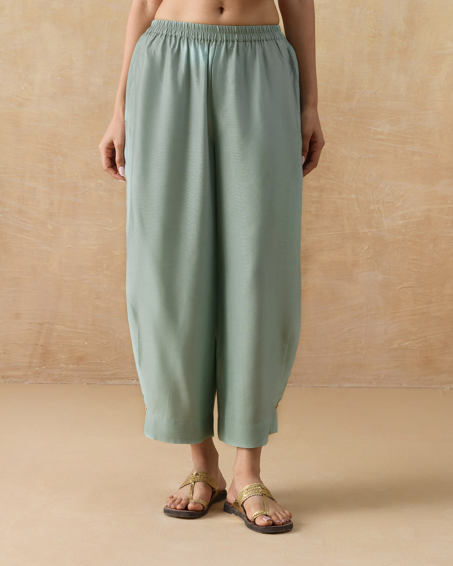 The Wander Pants, regular-fit aqua silk blend pants gathered at the hem, worn with flat sandals.