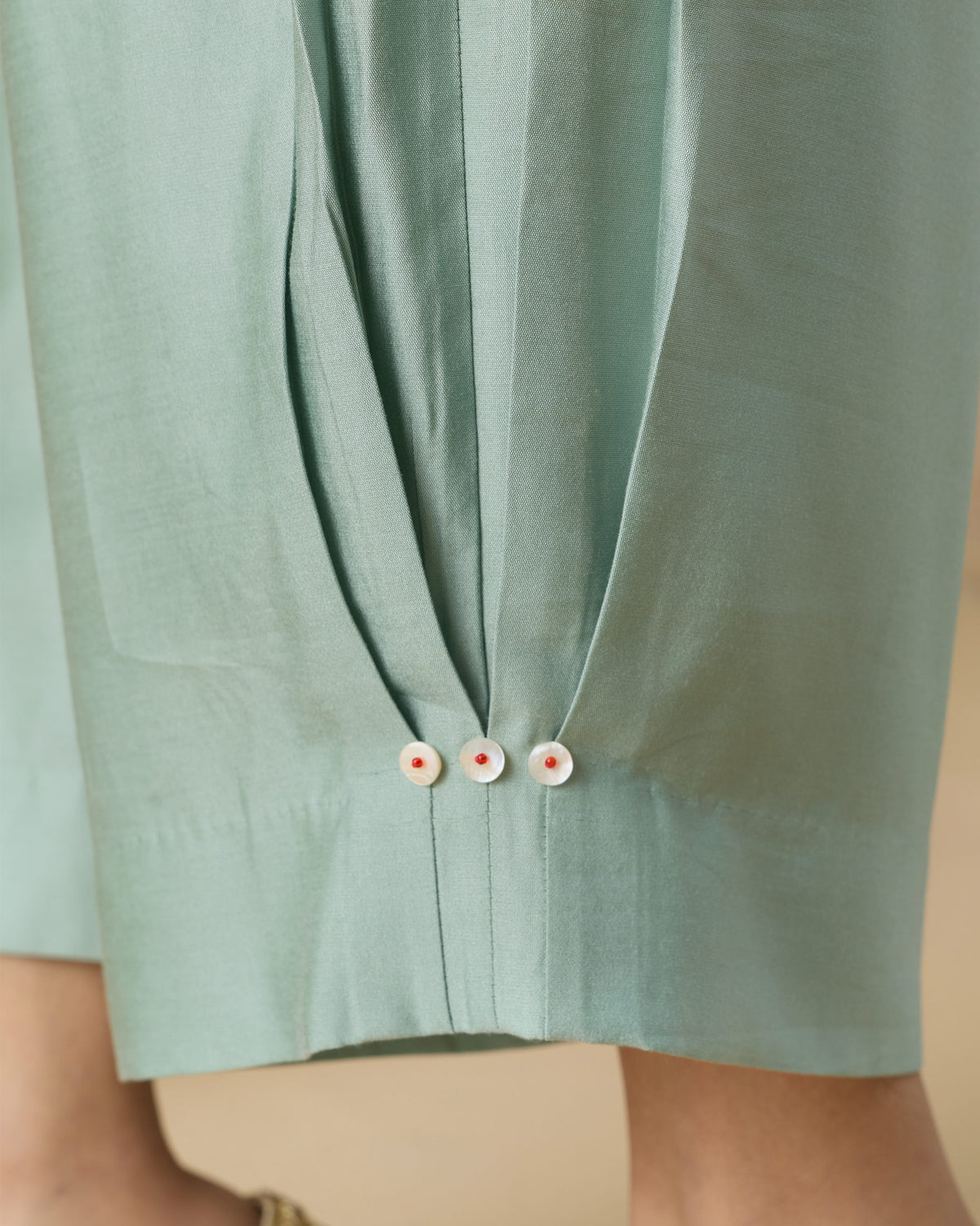 Close-up of pale green Wander Pants hem showing three white buttons with red centres.