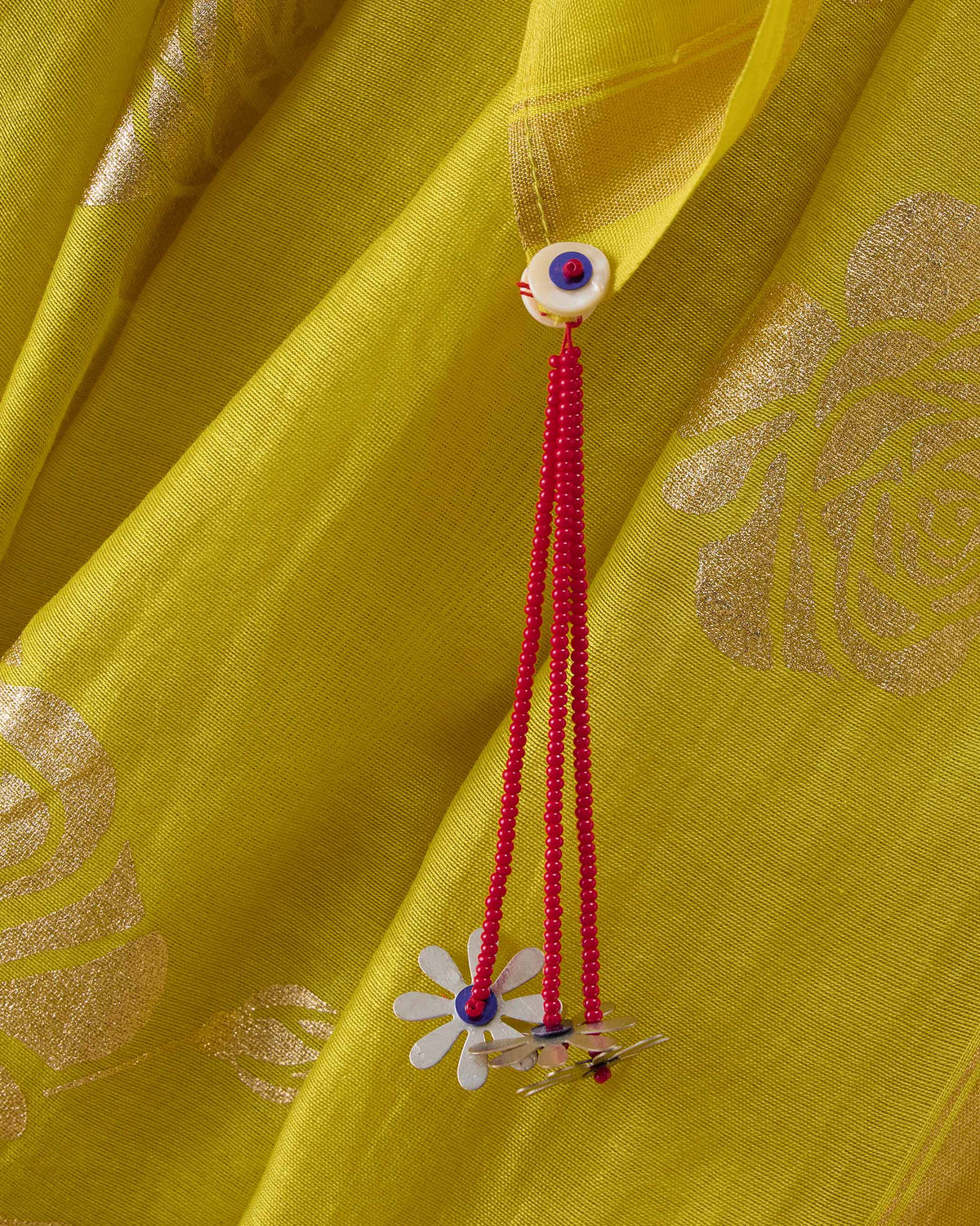 Close-up of gold foil roses and a red beaded tassel on chartreuse Sunset sari fabric.