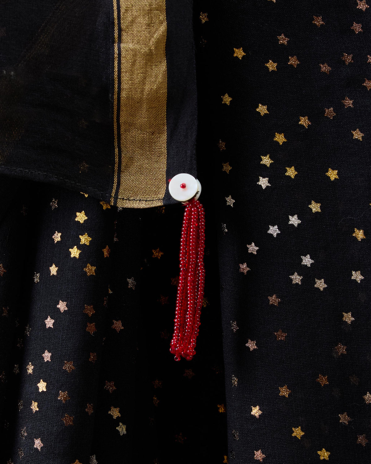 Close-up of gold stars and a red beaded tassel on a black Riverbank sari.