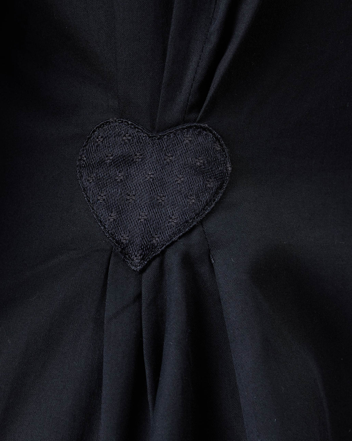 Close-up of a black heart appliqué on a black Rai top.
