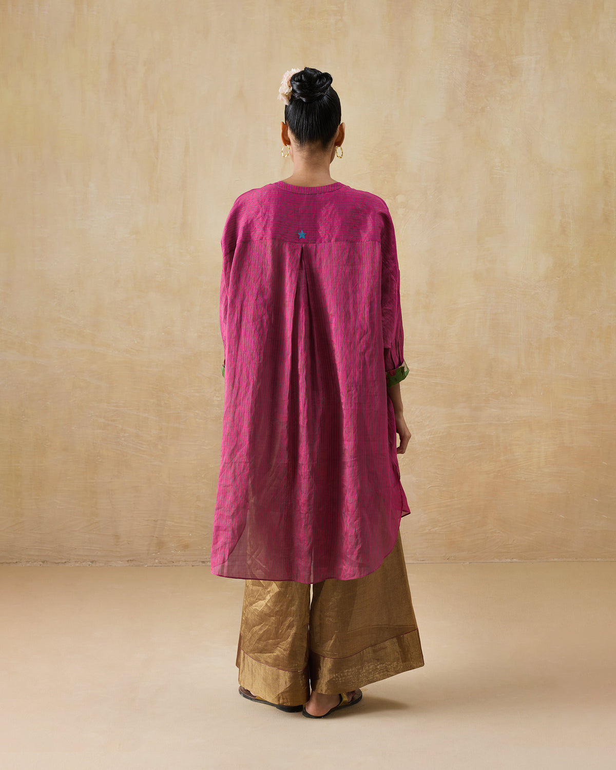 Back of a fuchsia Lazy Sunday tunic with a box pleat and blue embroidered star.