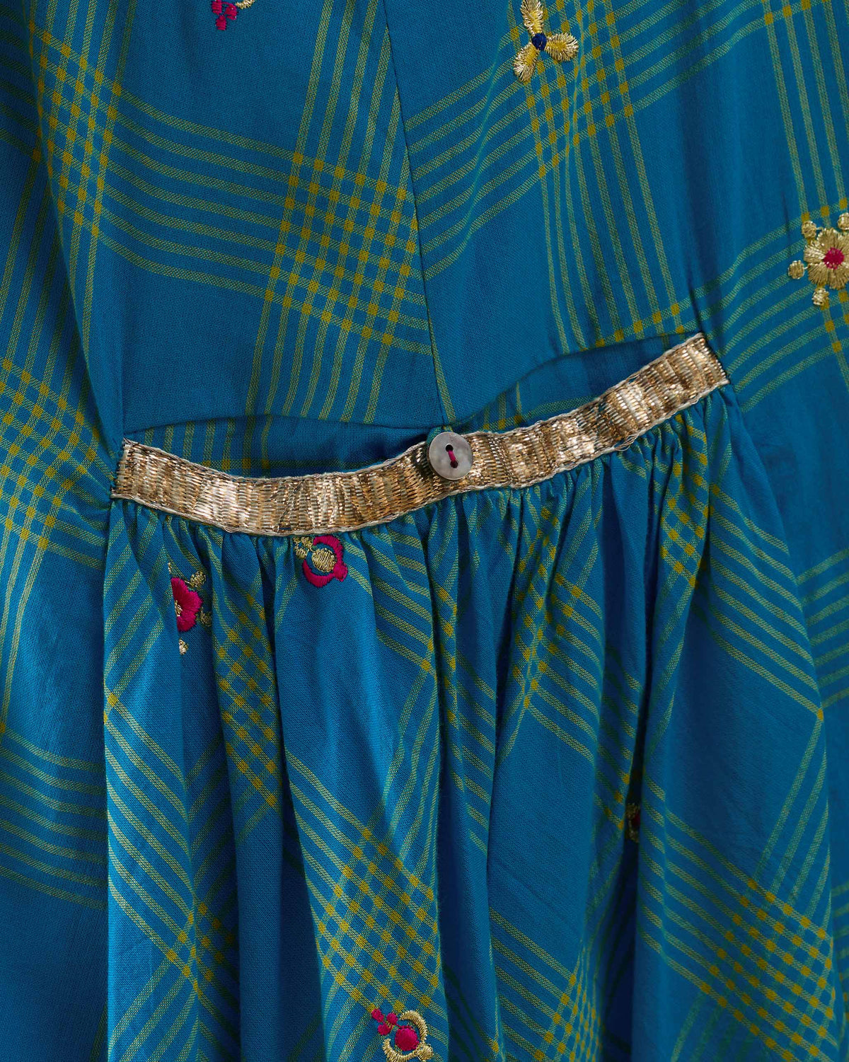 Close-up of gold waist trim and gathers on a cerulean check Nimbus dress.
