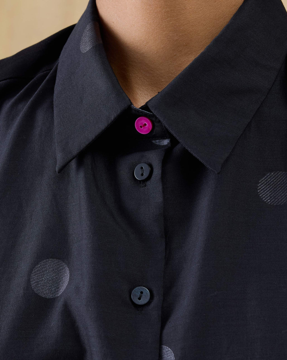 Close-up of a pink button on a black Sonnet dress collar.