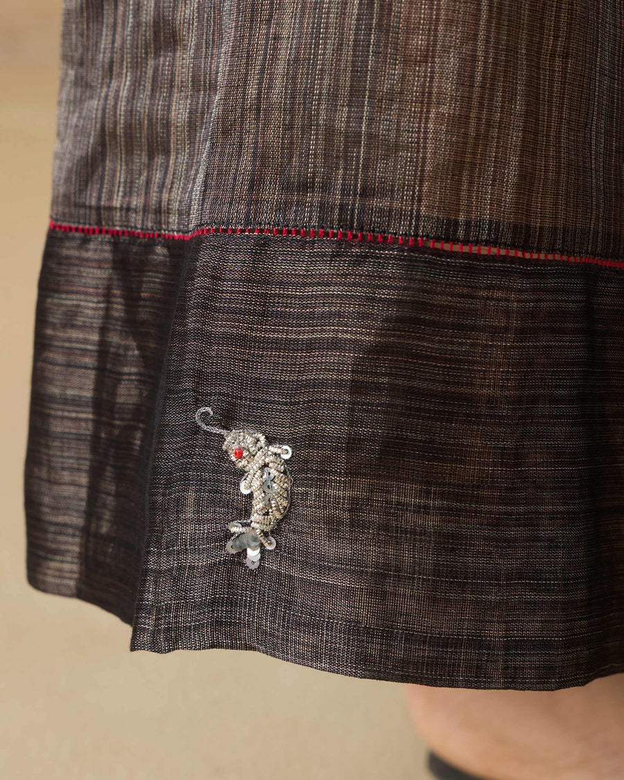 Close-up of the hem band of the Charisma Pants, joined with red fagotting, with a silver zardozi fish.