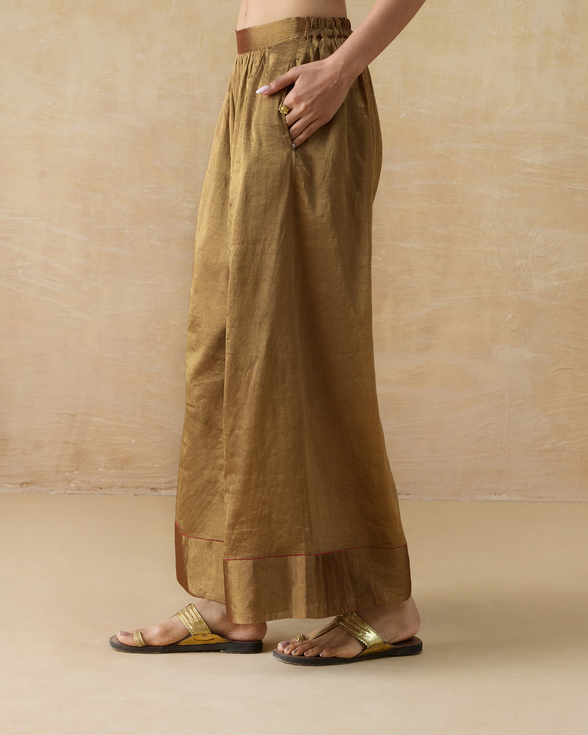 Side view of gold metallic Charisma pants with a side pocket.