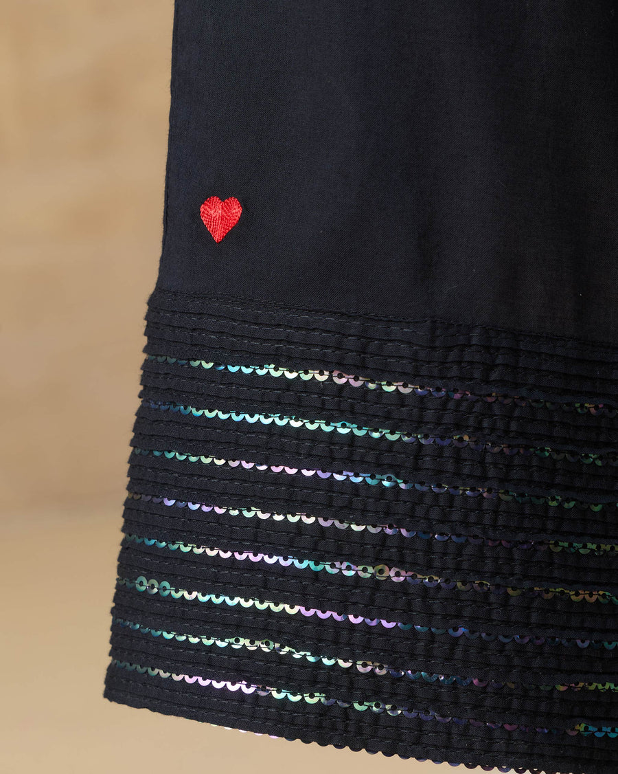 Close-up of the hem of the Stellar Pants, with a red heart above rows of black rainbow sequin pintucks.