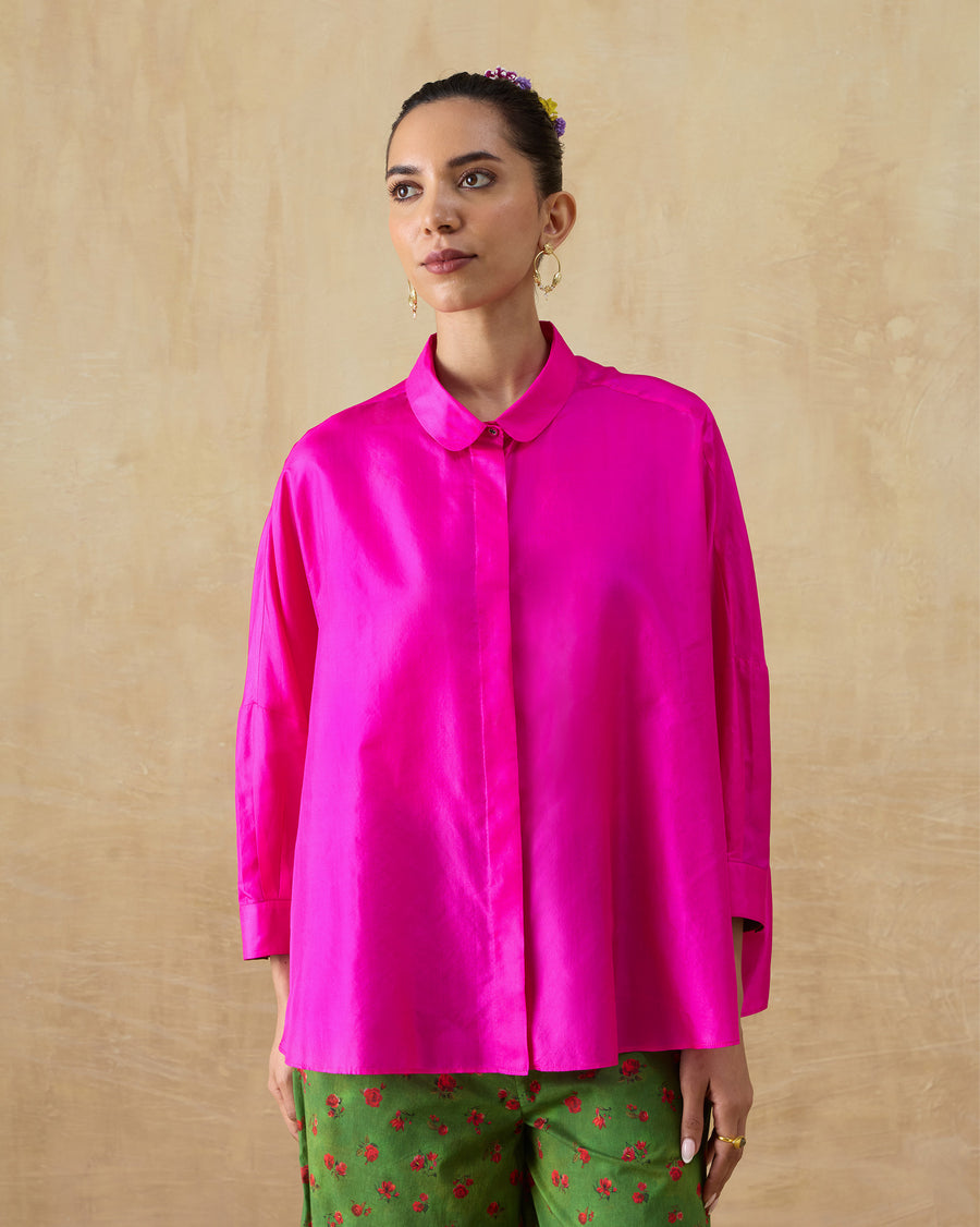 The Boxy Shirt, a loose fuchsia silk shirt with a rounded collar, worn with green printed trousers.