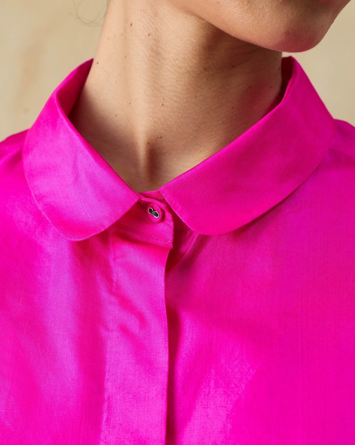Close-up of the rounded collar and top button on a fuchsia pink silk boxy shirt.