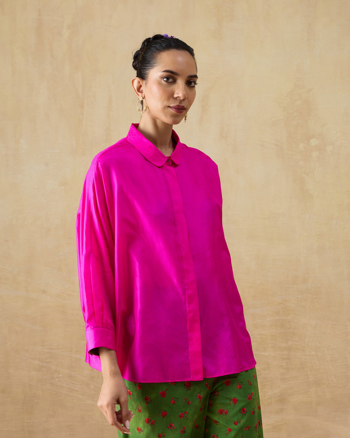 Person wearing a fuchsia pink silk boxy shirt with wide cuffs and a clean placket.