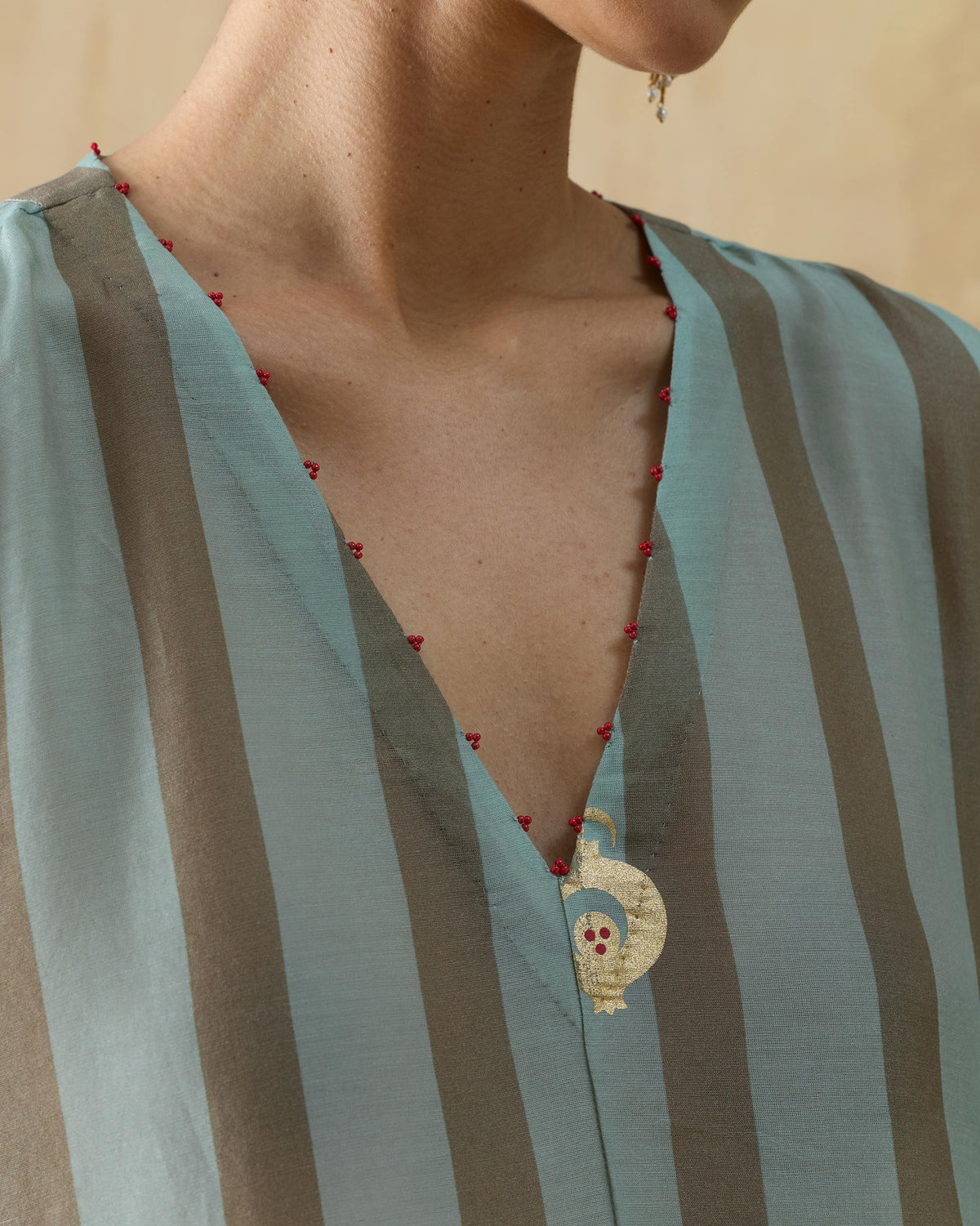Close-up of a Midnight Club kurta V-neck with red bead trim and a gold motif.