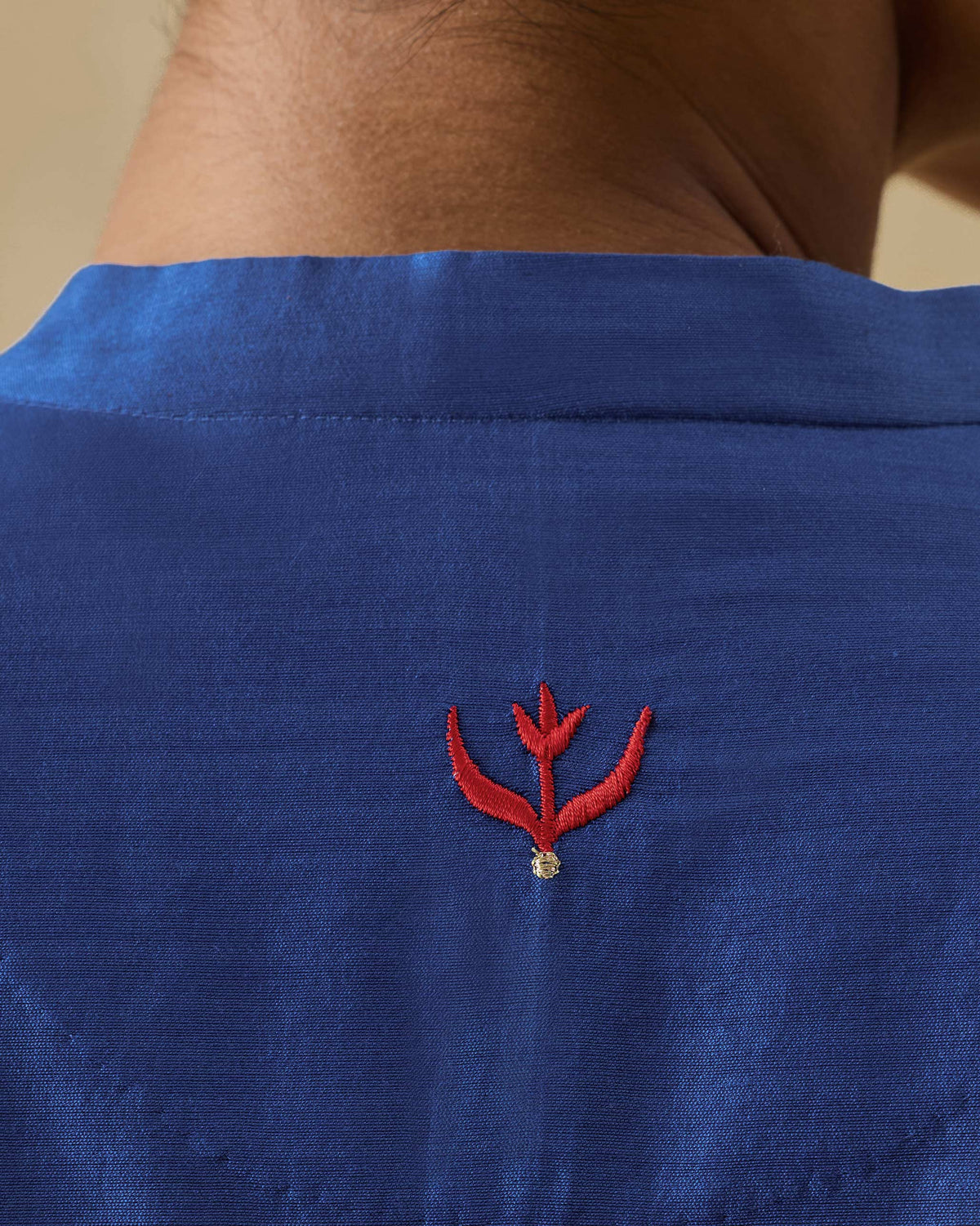 Close-up of a red embroidered motif on the back of a cobalt Moonsong kurta.