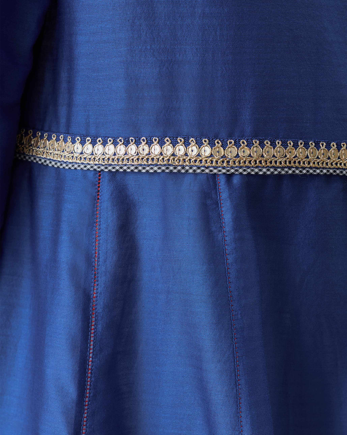 Close-up of gold waist trim and red stitching on a cobalt Moonsong kurta.