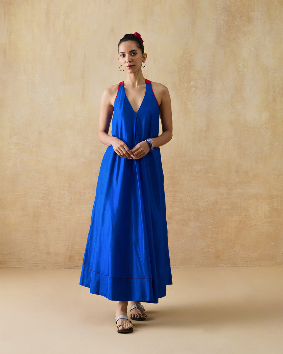 The Akira Twist Back Dress, a long cobalt blue silk halter dress with an A-line shape, worn with flat sandals.
