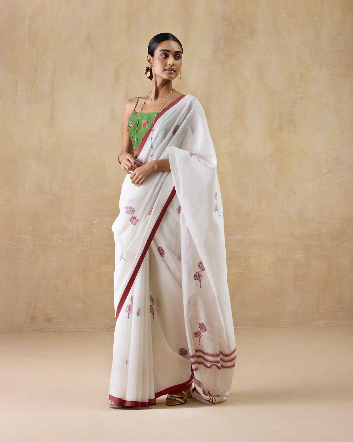 Ivory cotton silk Stardust sari with pink floral print and red border, worn by a person.
