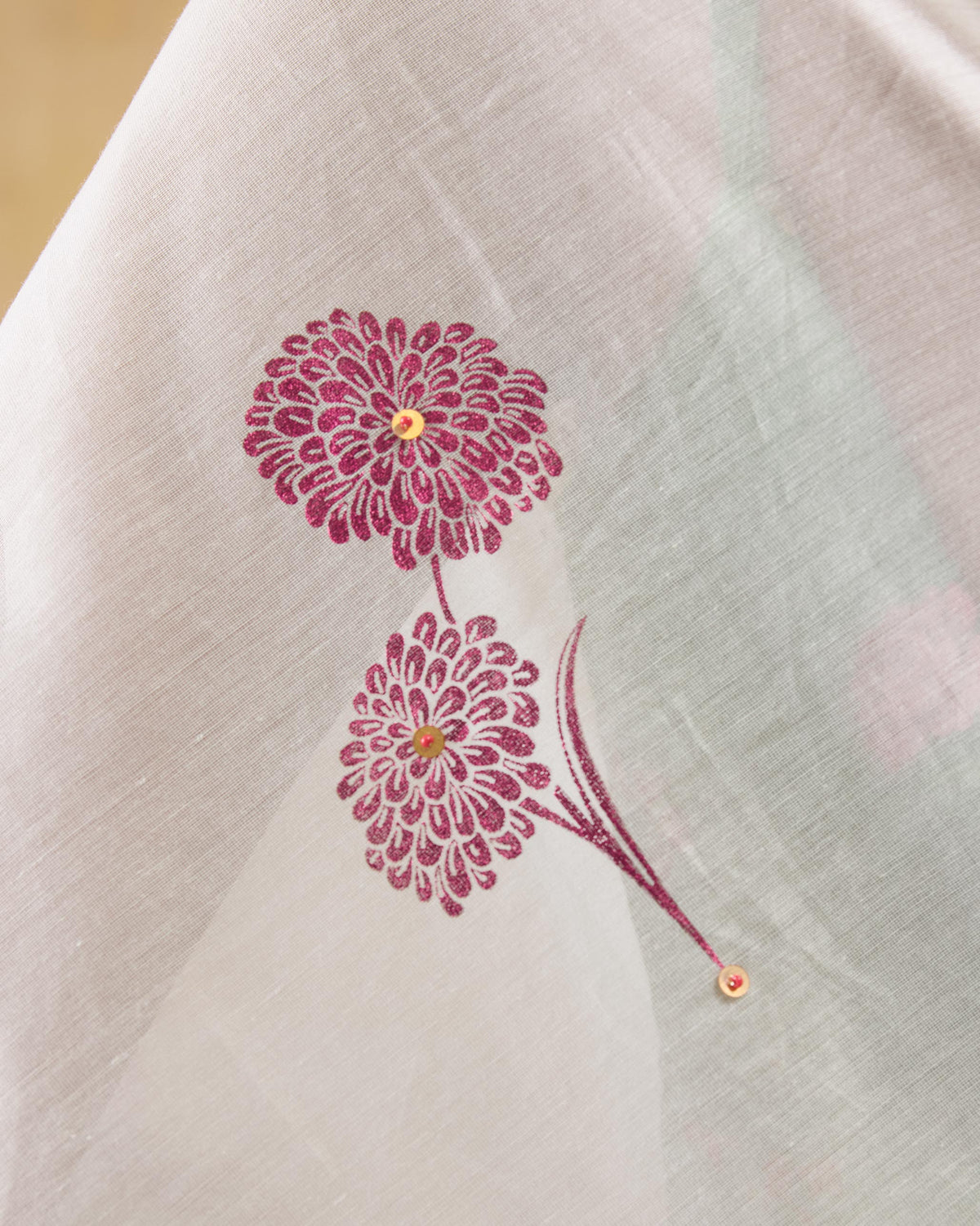 Close-up of pink genda flower foil print with gold sequins on ivory Stardust sari fabric.
