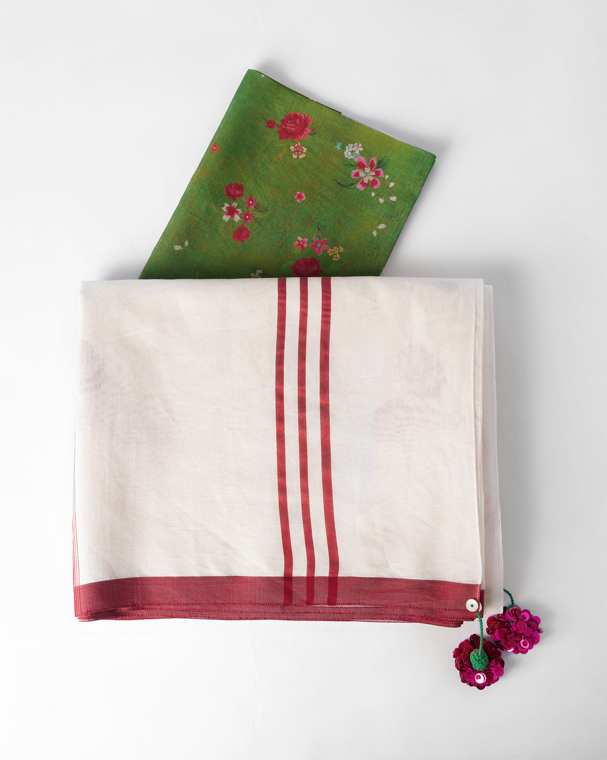 Folded ivory Stardust sari with red border, sequin tassels and a green floral blouse piece.