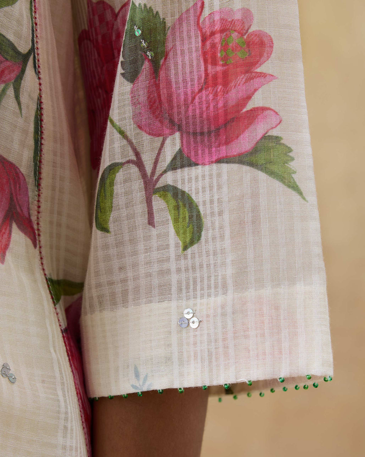 Close-up of an ivory kurta sleeve with roses and green bead trim.