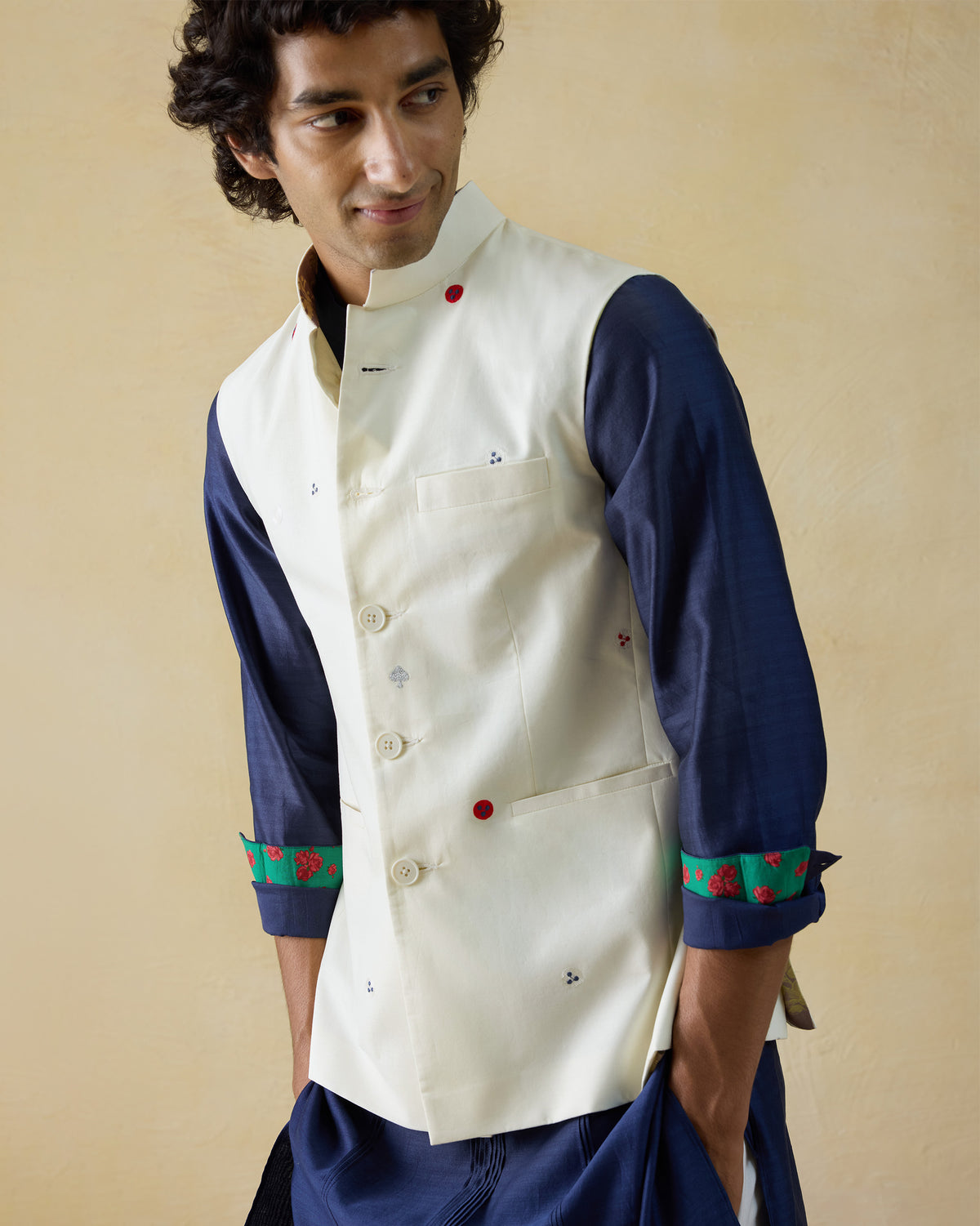Person wearing an ivory Nehru Jacket with red embroidered dots over a navy kurta.