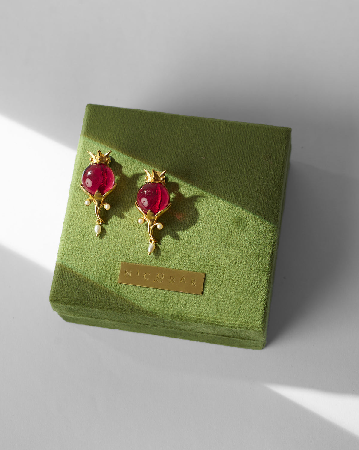 Pair of gold Pom Pearl Drops with red stones on a green gift box.