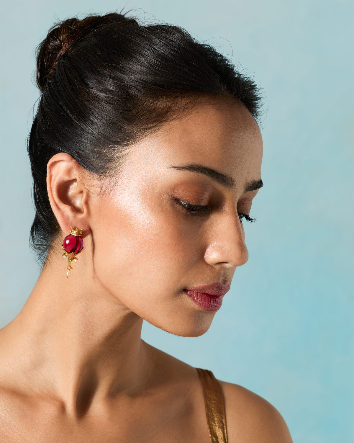 Person wearing gold Pom Pearl Drops with a red stone.