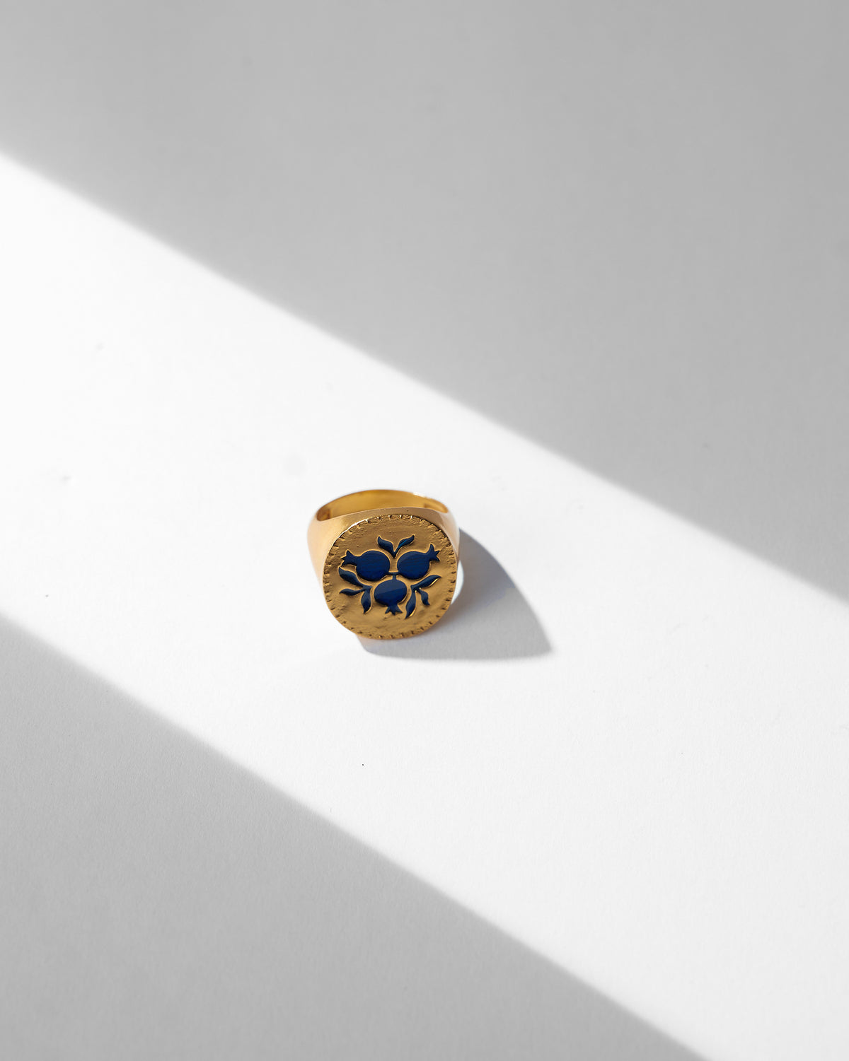 Gold Anar ring showing a navy enamel pomegranate cluster on a round face.