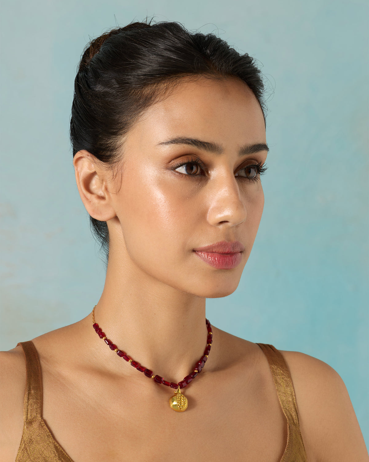 Person wearing a gold Anar Bagicha necklace with a pomegranate pendant.
