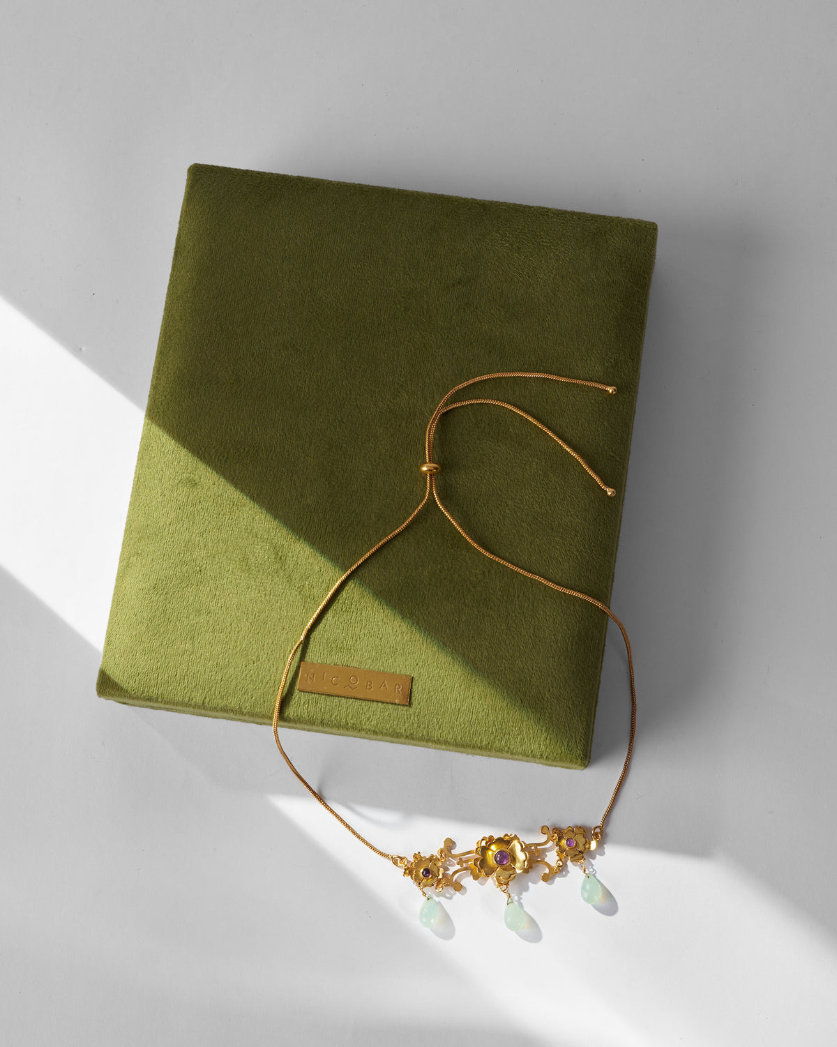 Gold Kesar choker with pale green drops laid on a green box.