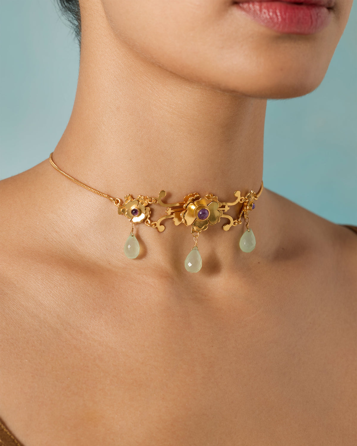 Person wearing a gold Kesar choker with pale green drops.
