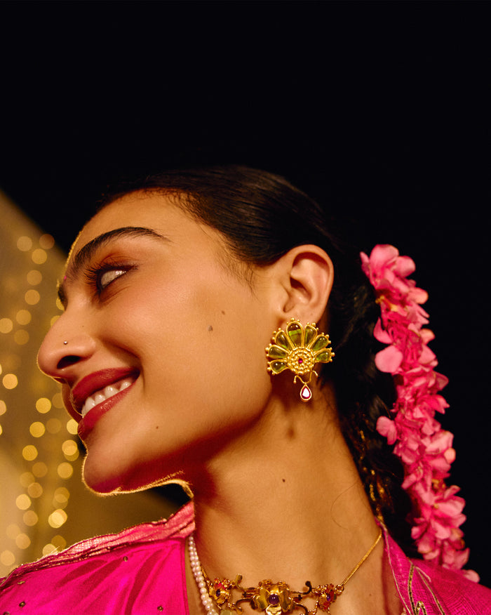 Person wearing a gold Mari-Palm earring with green petals and a pink drop.
