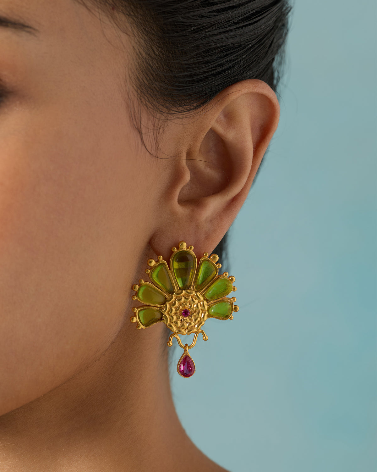 Close-up of a gold Mari Palm earring with green glass petals and a pink drop worn on an ear.