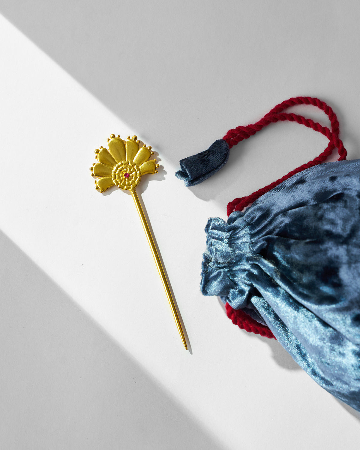 Gold Mari-Palm hairpin beside its blue velvet pouch.