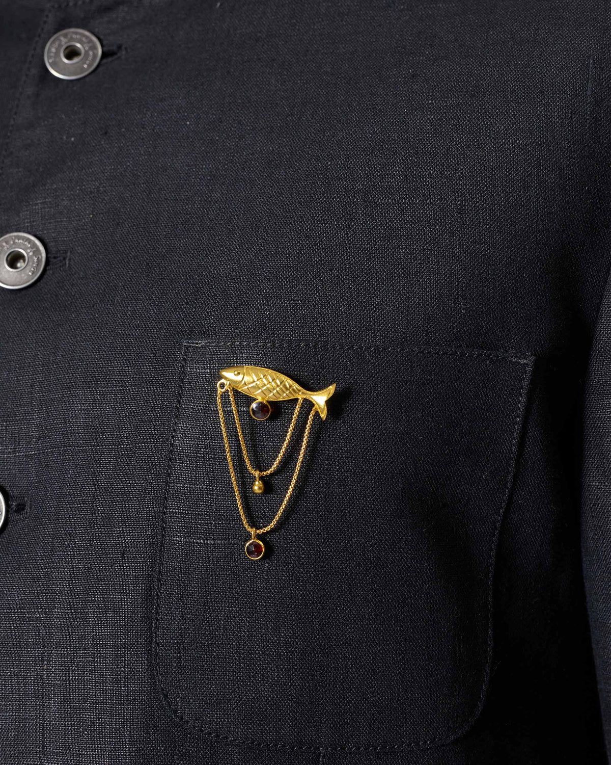 Close-up of a gold Masse Pin with a fish motif on a jacket pocket.