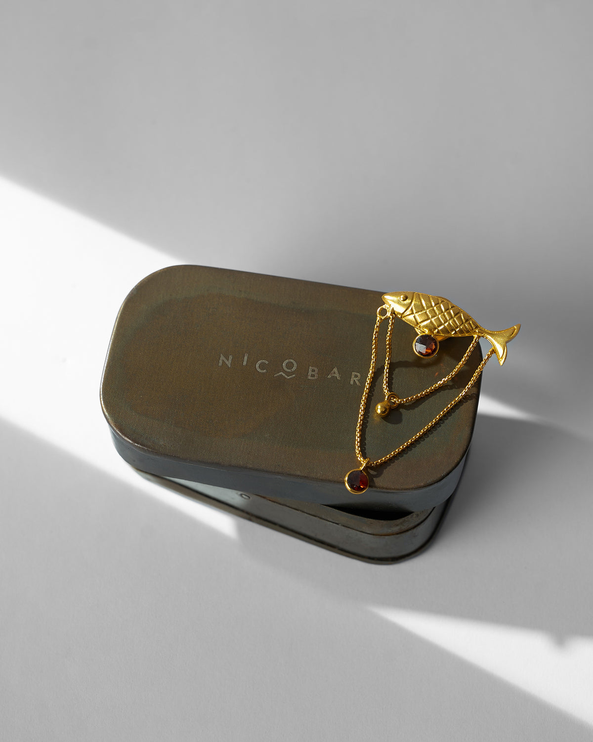 Gold Masse Pin with a fish motif resting on a Nicobar tin.