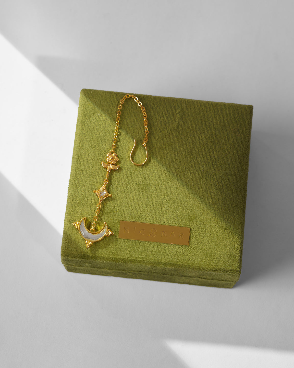 Gold Chand maangtika with crescent mirror on a green Nicobar gift box.