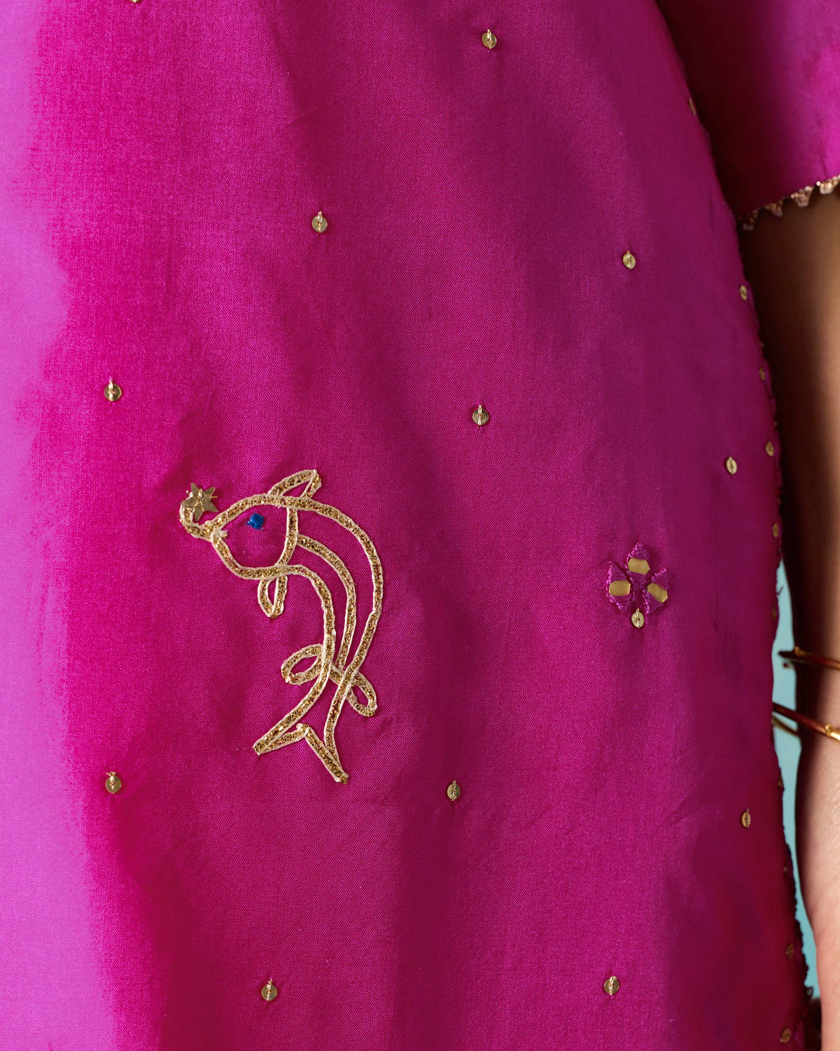 Close-up of a gold fish motif embroidered on a magenta Milni kurta.