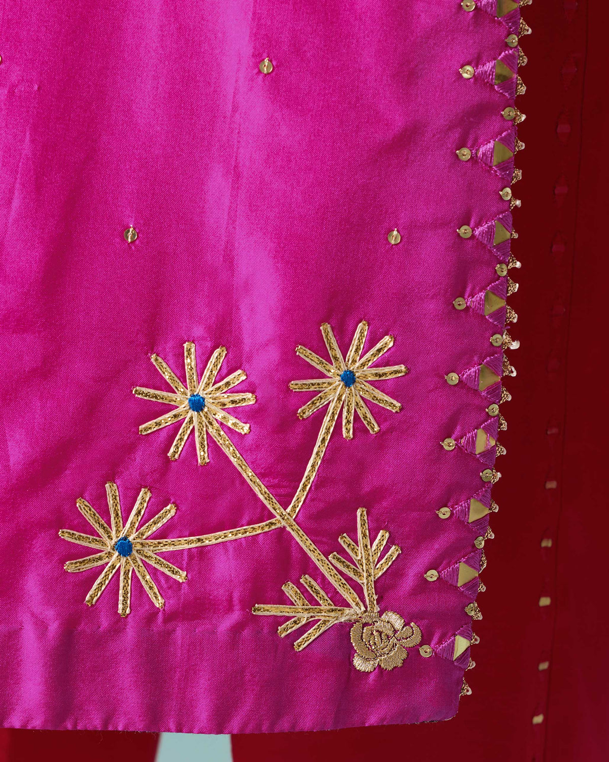 Close-up of gold flower embroidery on the hem of a magenta Milni kurta.